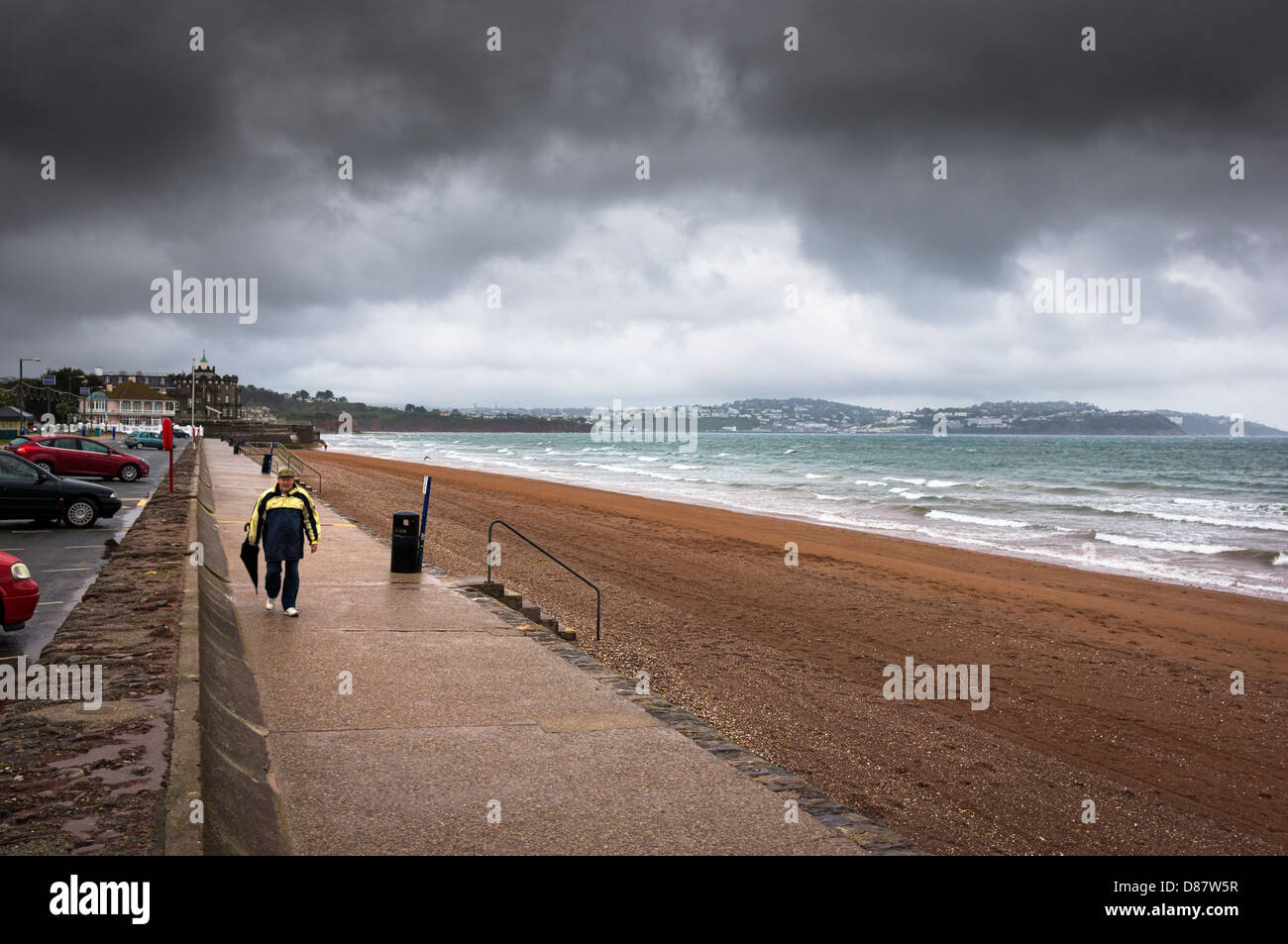 Tempesta - uomo che cammina ai margini della spiaggia di Paignton in una tempesta di pioggia in un giorno di pioggia, Inghilterra, Regno Unito Foto Stock