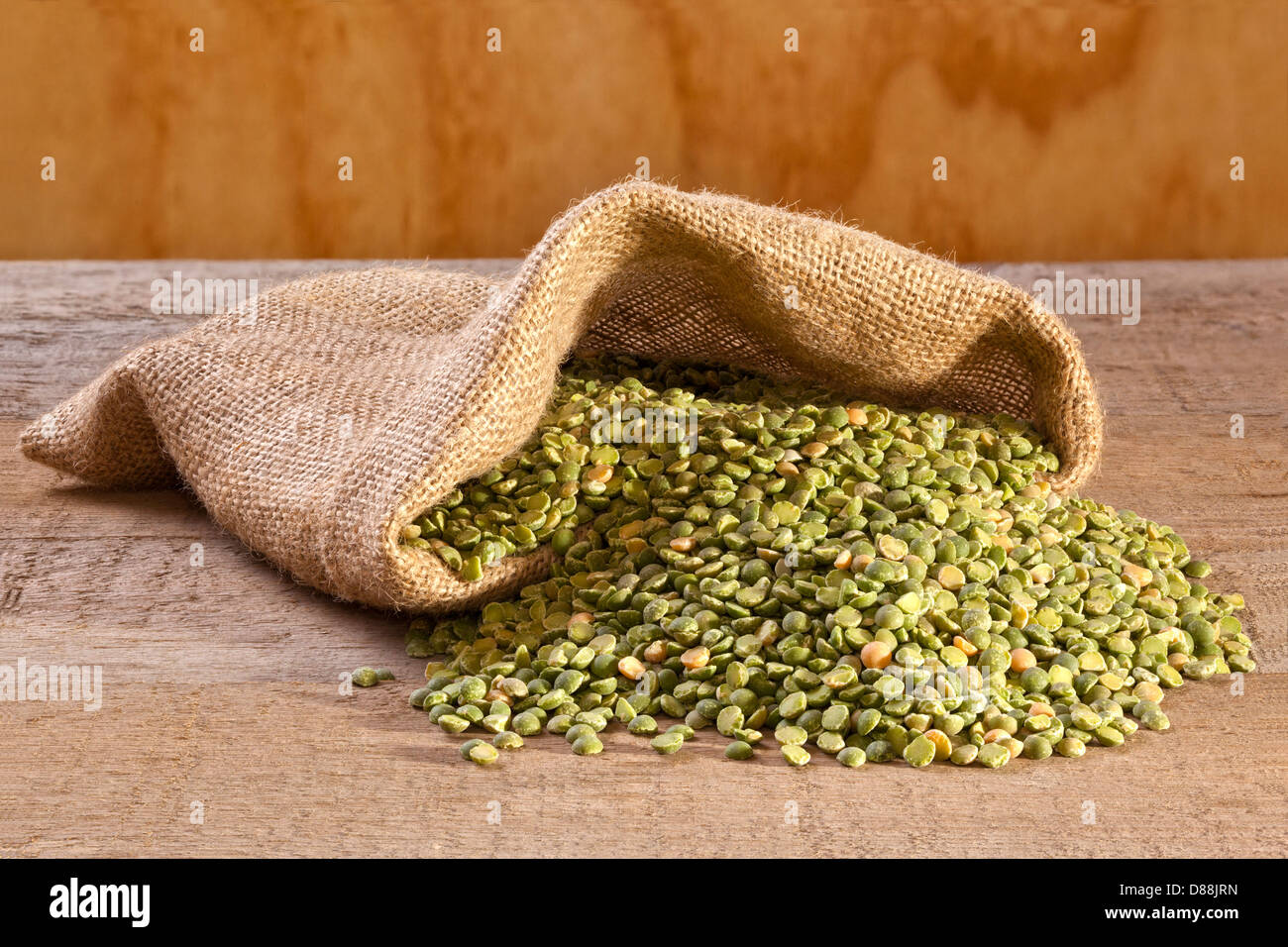 Split piselli verdi fuoriuscita da una tela o sacco di iuta, su un listone rustico sfondo. Foto Stock