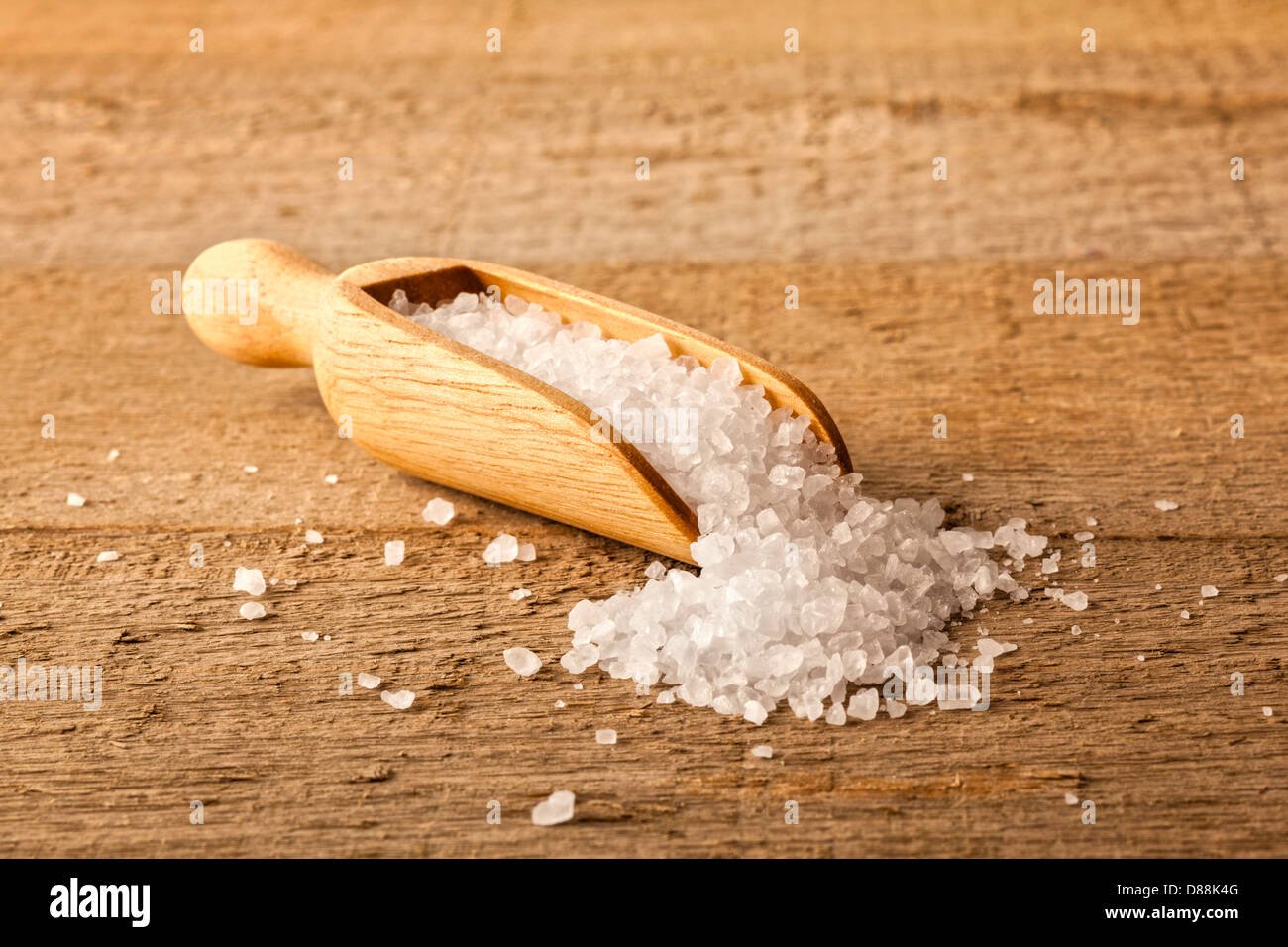 I cristalli di sale in un Scoop - un piccolo cucchiaio di legno riempita con cristalli di sale che sono spargimento su un rustico di una superficie di legno. Foto Stock