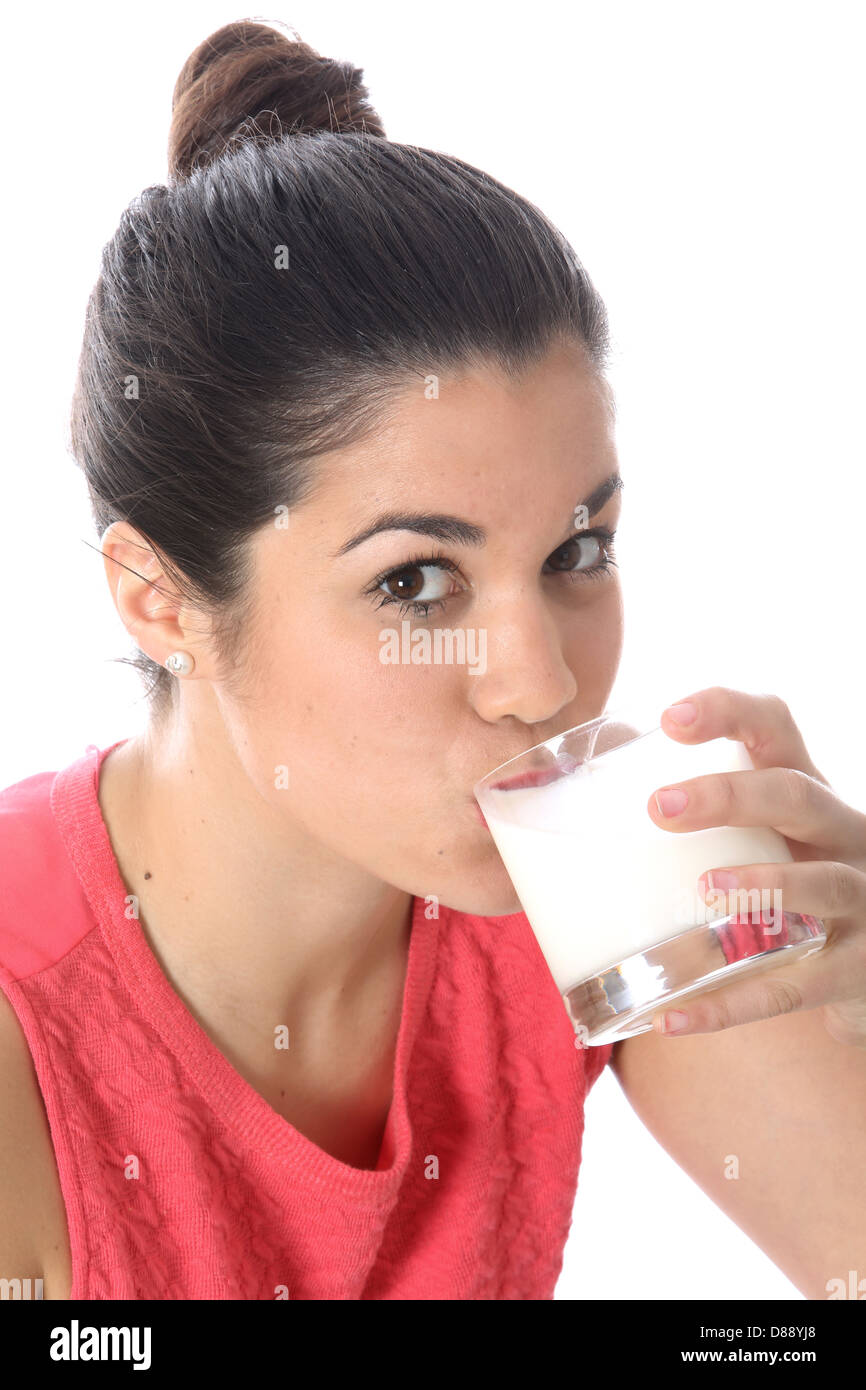 Giovani dai capelli scuri donna europea Holding e bere un bicchiere di fresco latte sano contro uno sfondo bianco con i suoi capelli legati a Bun Foto Stock