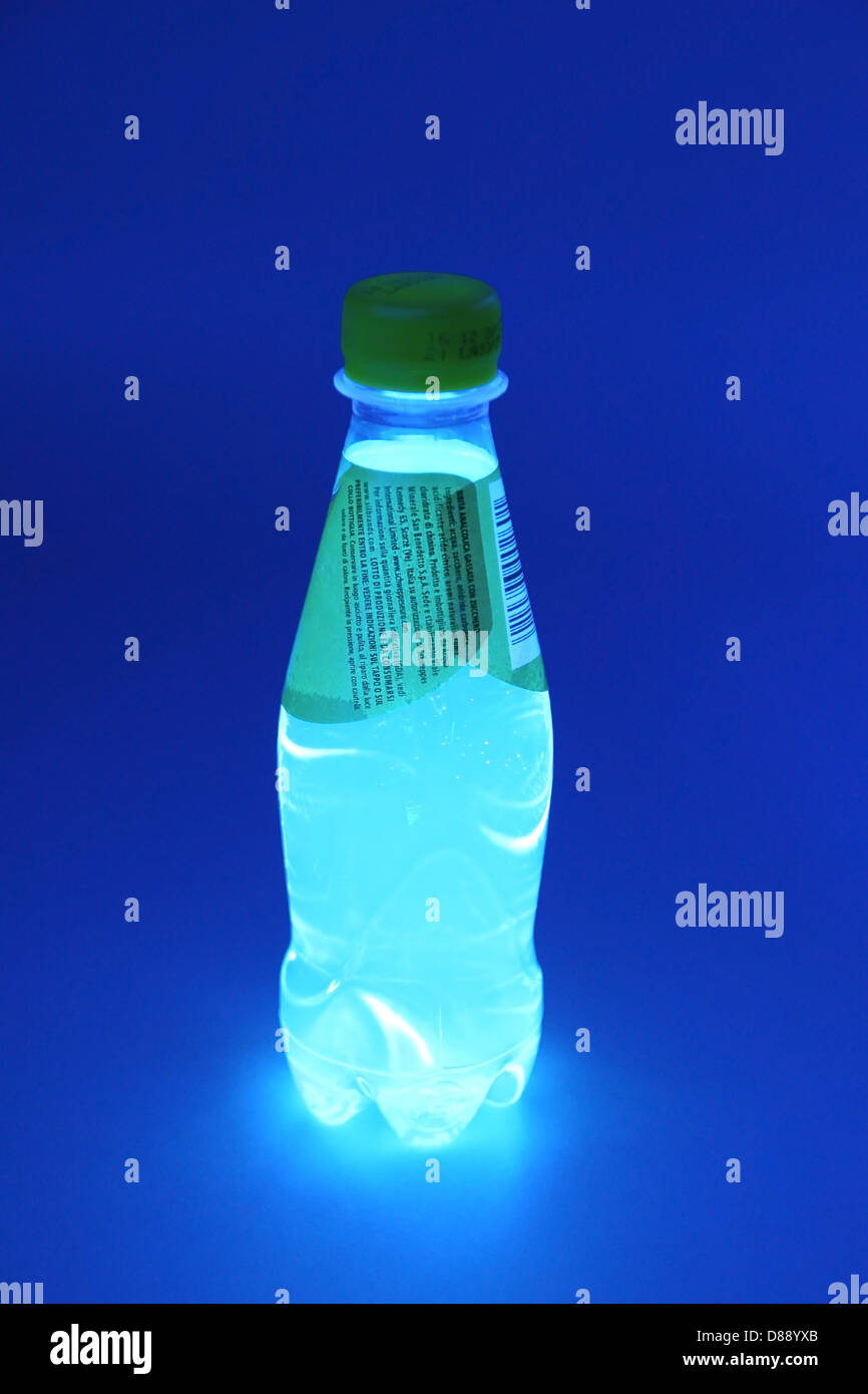 Piccolo senza marca acqua tonica bottiglia ultravioletto sotto luce UV. La bottiglia è incandescente come chinina contenuto in acqua tonica fluorescente Foto Stock