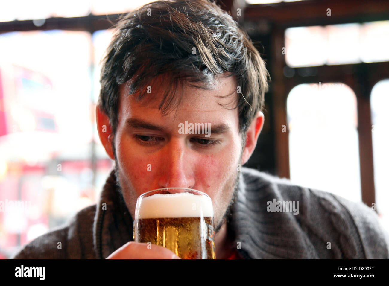 Un uomo prende un sorso al di fuori di un appena spillata lager in un pub Inglese. Il leone nero, Kilburn Foto Stock