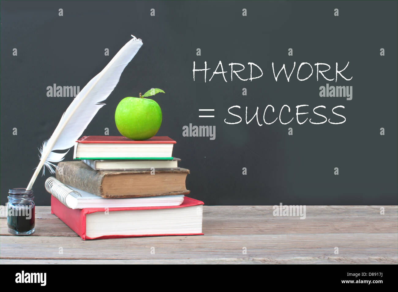 Hard work is success written on a blackboard with a pile of books, quill and ink Foto Stock