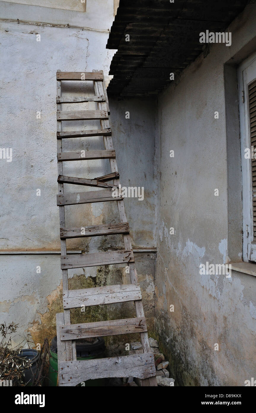 Rotto in legno scaletta appoggiata contro la parete di pelatura della casa abbandonata. Foto Stock