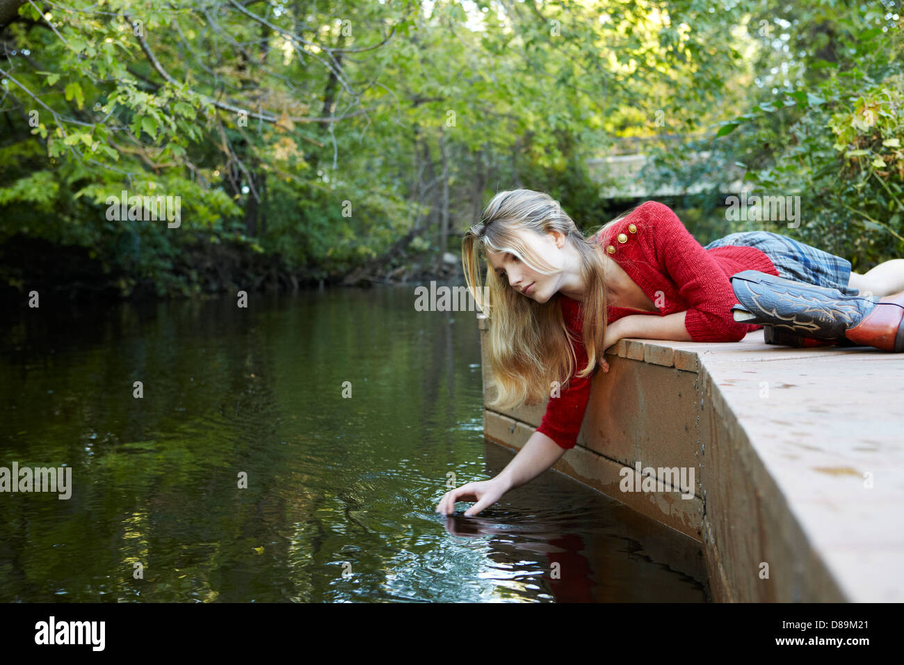 Teen sul dock trailing la sua mano nell'acqua Foto Stock