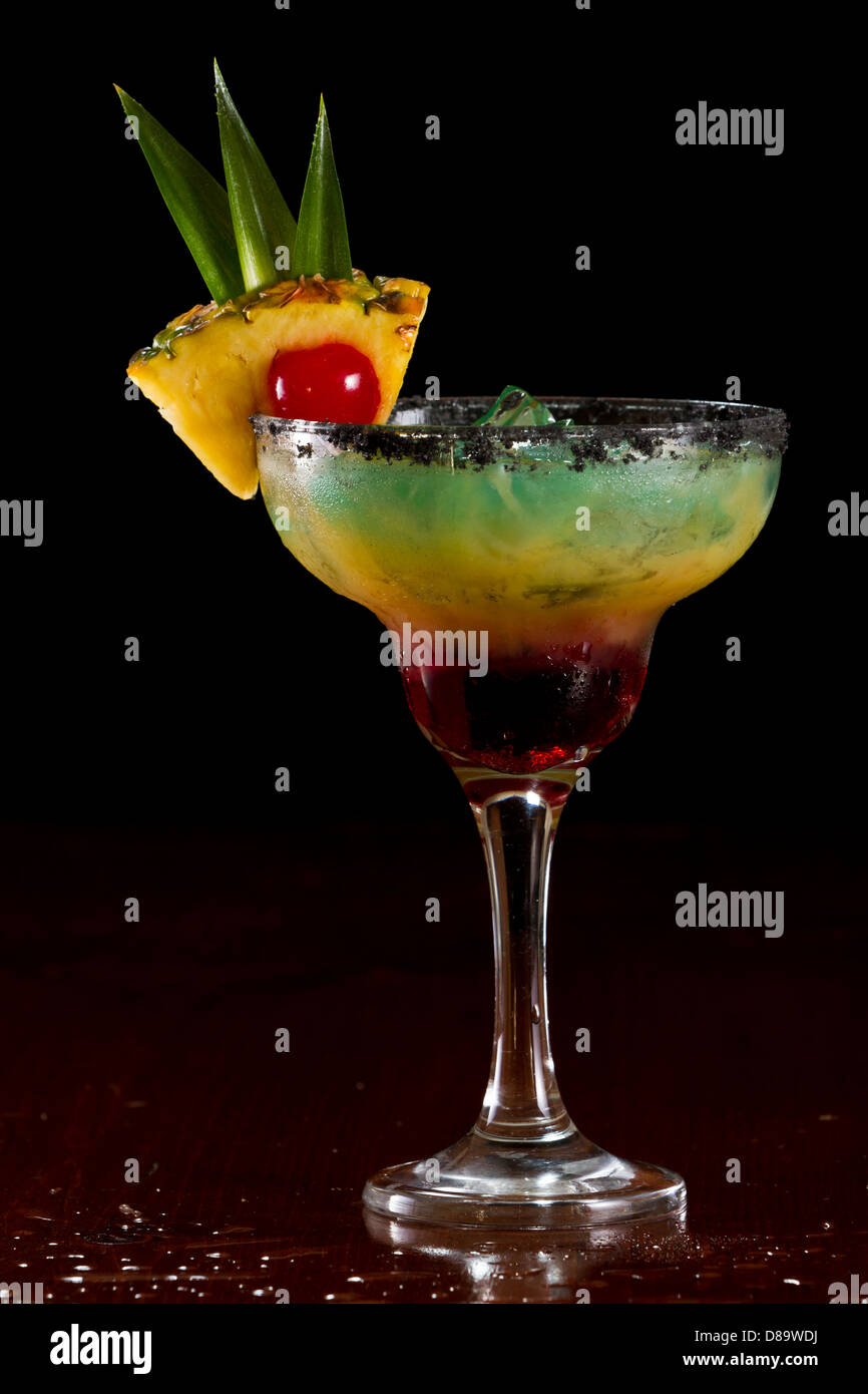 Bella tropical cocktail servito in un bicchiere Margarita con sale nero sul cerchio e una fetta di ananas con una ciliegia in esso Foto Stock