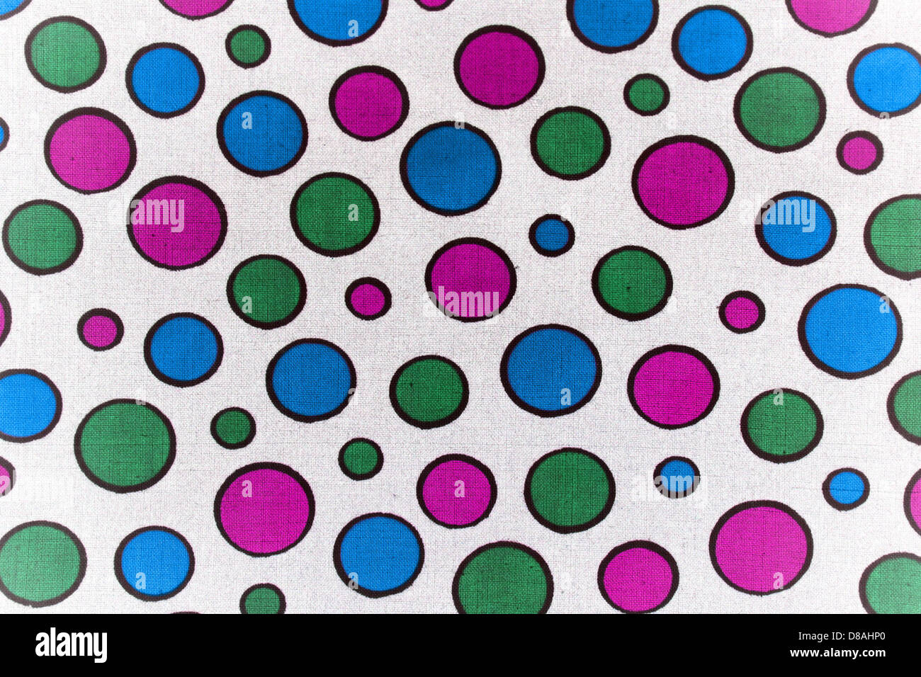 Un'immagine ravvicinata di tessuto bianco con un motivo giocoso di punti blu, rosa e verdi. La texture è liscia, evidenziando i colori vivaci dei punti contro la base in tessuto neutro, spesso utilizzato in tessuti casual o decorativi. Foto Stock