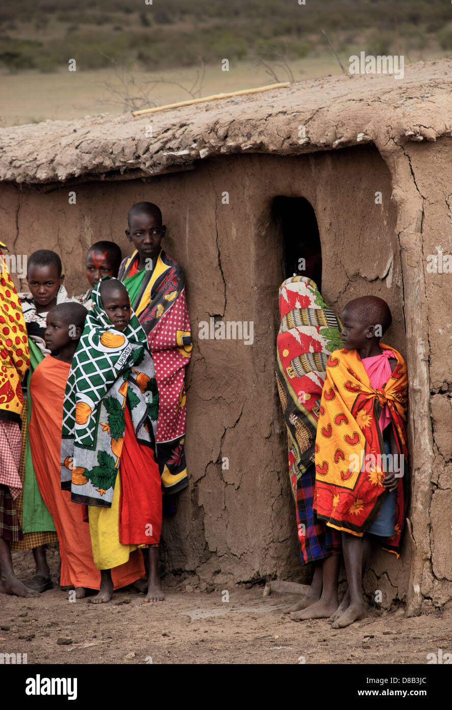 Masai bambini, indossando abiti tradizionali in piedi di fronte a una capanna di fango in un villaggio Masai Mara, Kenya, Africa Foto Stock