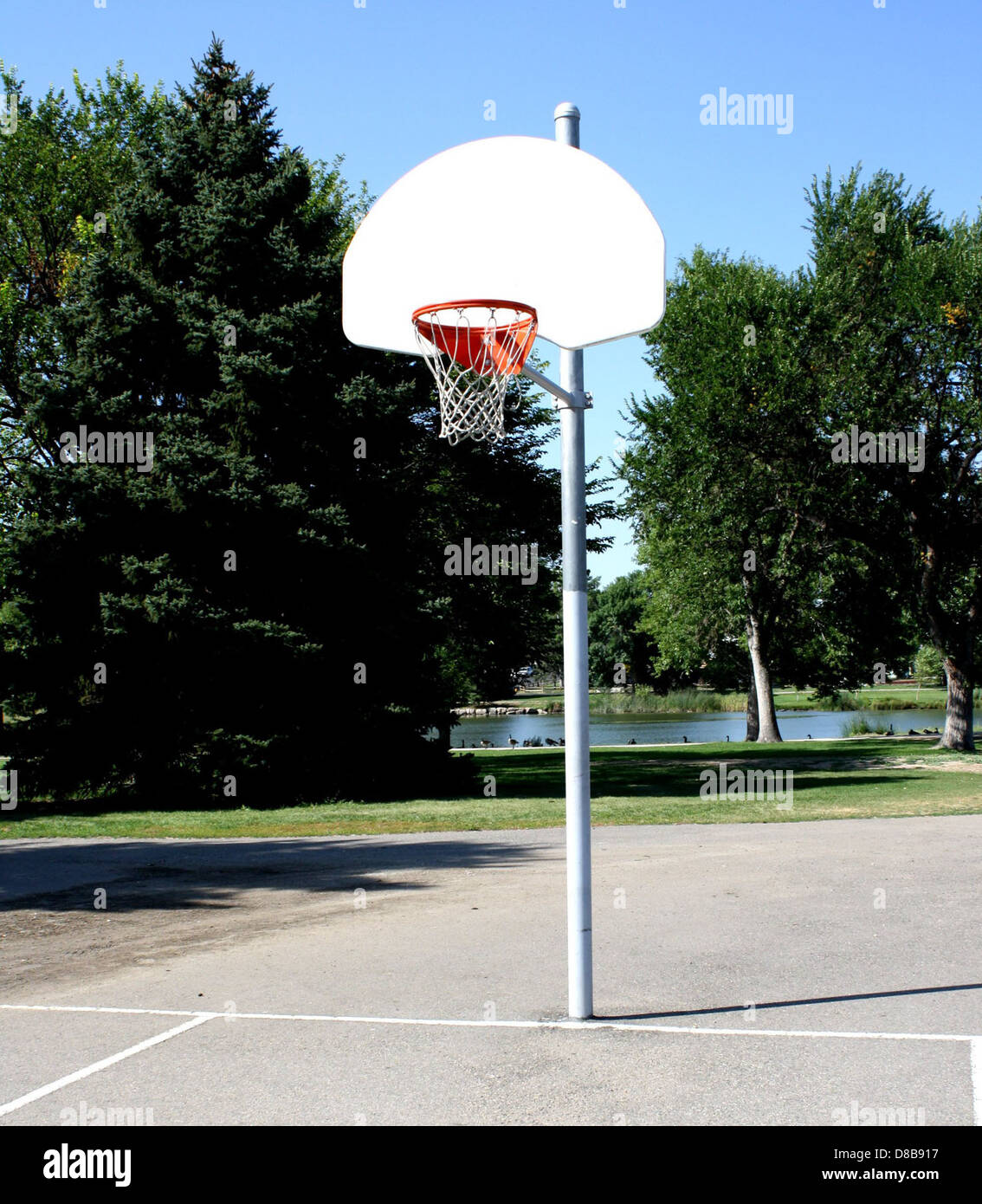 Un canestro da basket si trova in un parco pubblico, con un cielo limpido sopra e un campo aperto sotto. L'immagine mostra un luogo ricreativo comune per sport e attività all'aperto. Foto Stock