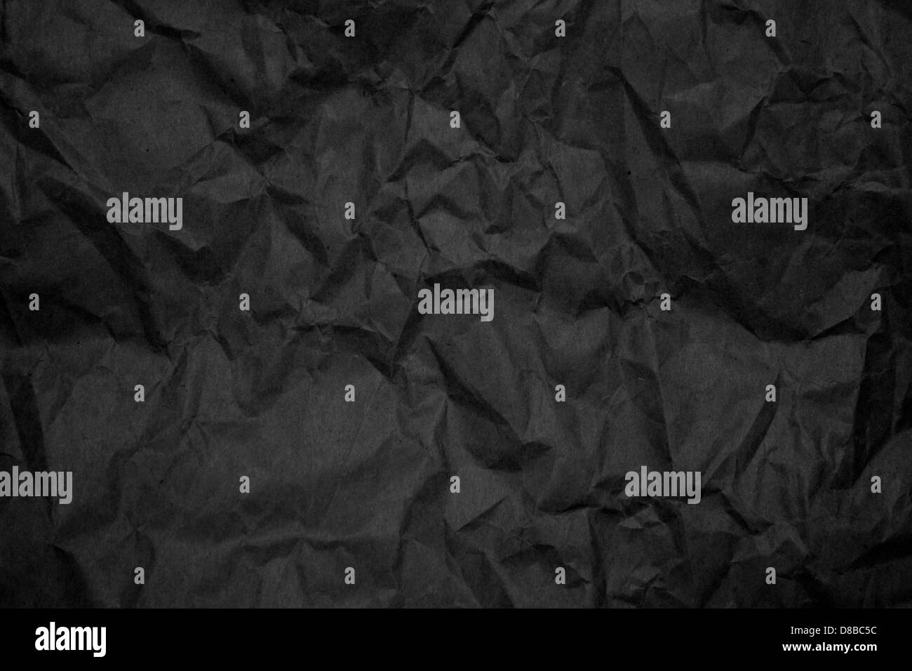 Un primo piano di carta nera increspata, che mette in risalto la trama e le pieghe intricate. L'immagine acquisisce il motivo irregolare e la profondità delle increspature sulla superficie della carta. Foto Stock