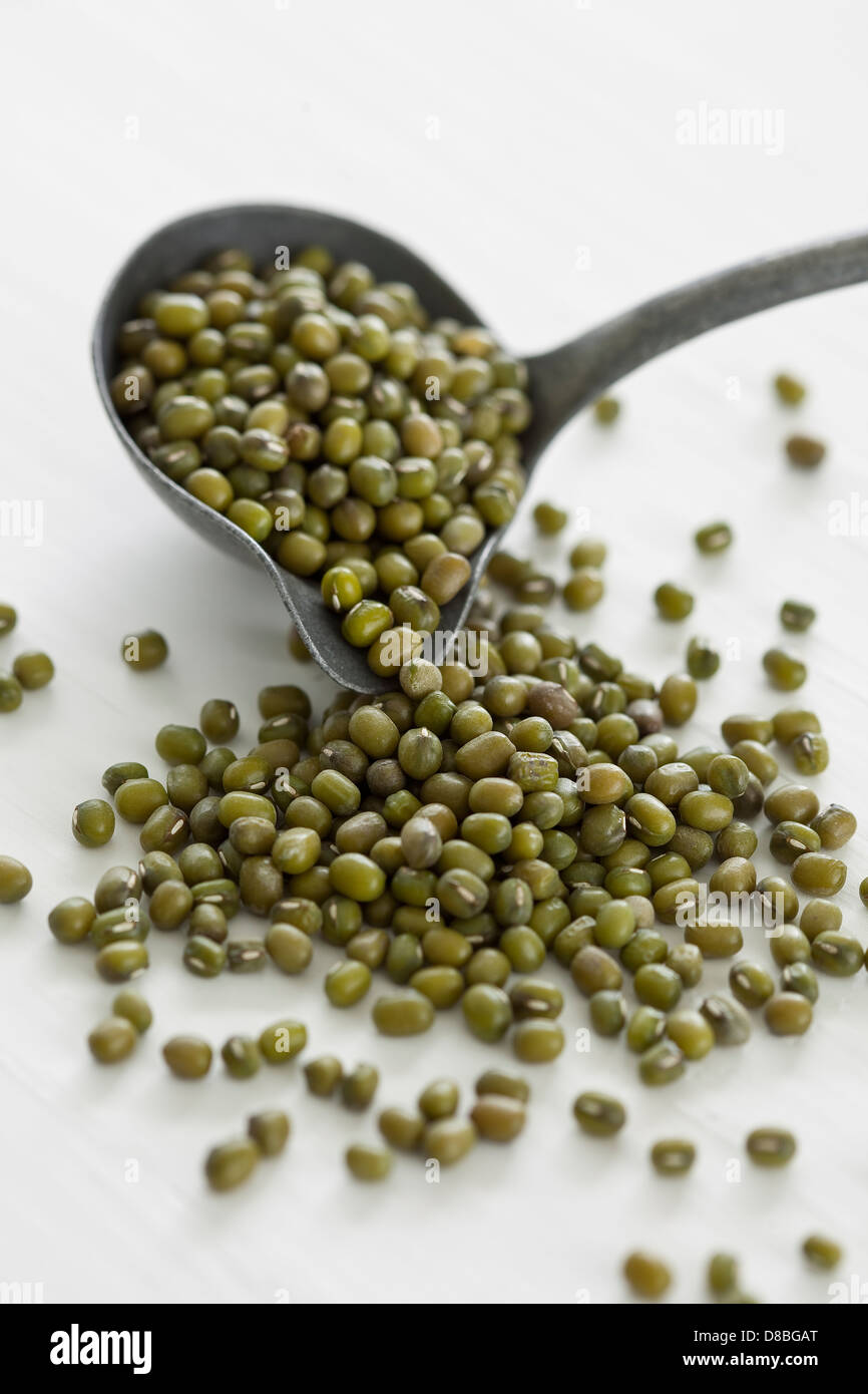 Il verde non cotti i fagioli mung fuoriuscita di una siviera su un bianco superficie di legno. Foto Stock