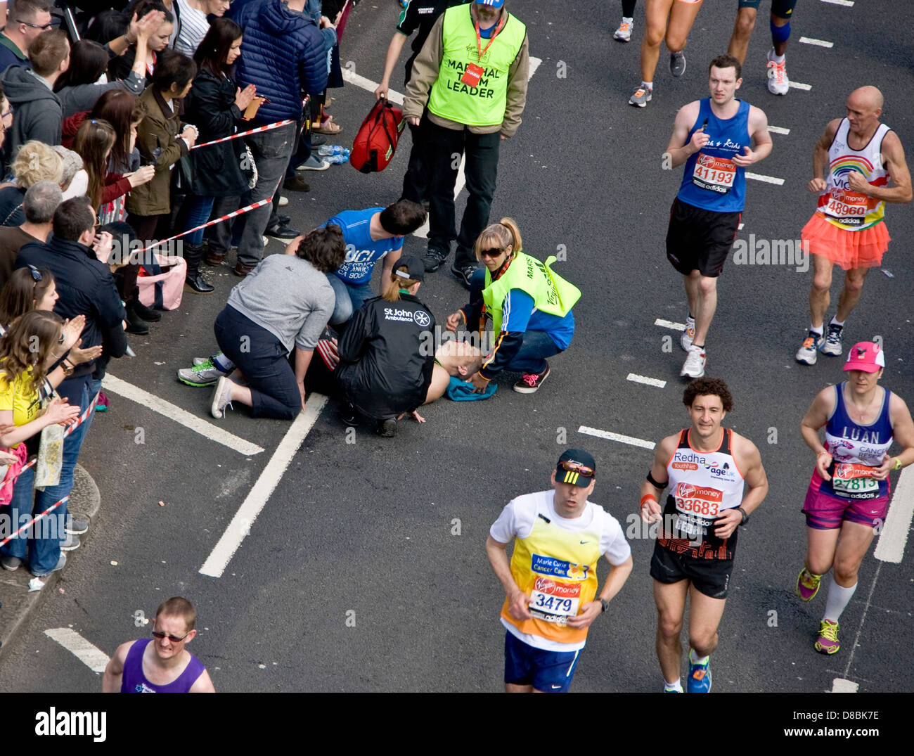 Gli ufficiali di gara e St John Ambulance guida è crollato un concorrente maschile nel 2013 maratona di Londra Victoria Embankment Inghilterra Europa Foto Stock