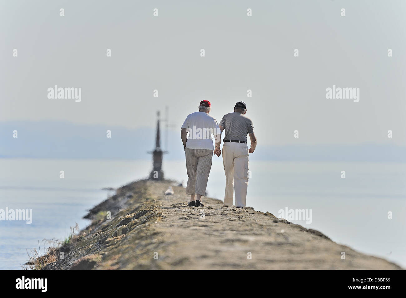 Una coppia di anziani tenendo le mani mentre si cammina su un molo sul lago Foto Stock