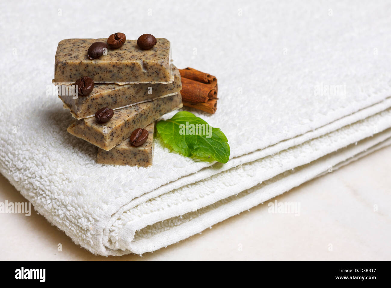 Pila di fatti in casa sapone aromatizzato bar circondato da caffè in grani, cannella e foglie di lavanda su asciugamano bianco. Foto Stock