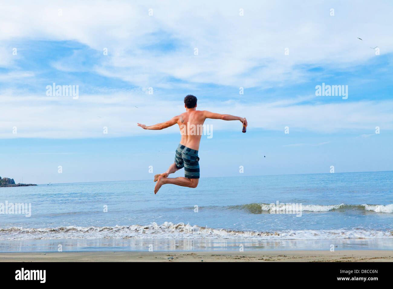 Uomo salta in aria sulla spiaggia Foto Stock