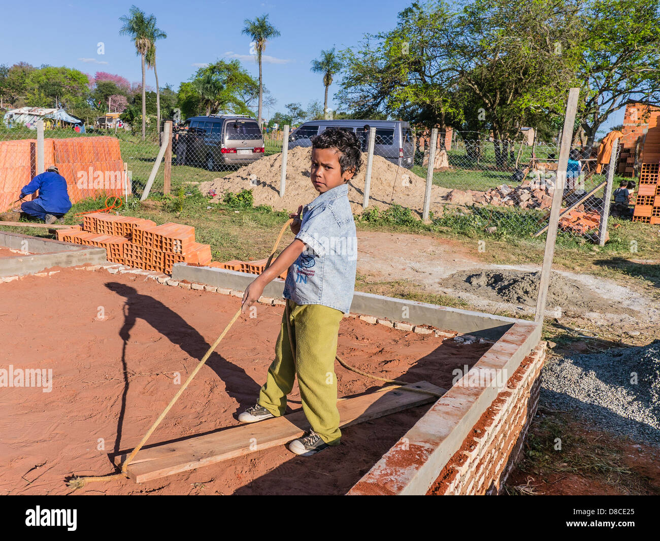 Un giovane paraguaiano ispanico boy guarda come egli tira su una fune fissata ad una trave di legno utilizzati nella compattazione del suolo. Foto Stock