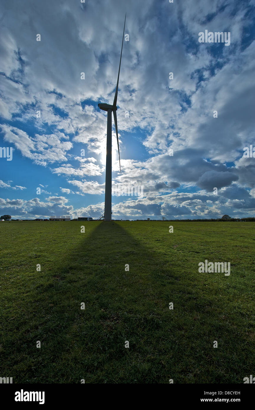 Una turbina eolica getta un ombra su un campo verde. Foto Stock