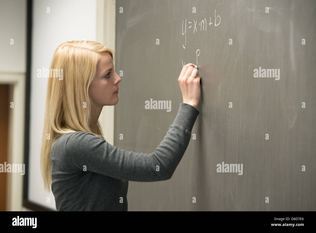 Studentessa in piedi nella parte anteriore della lavagna, la scrittura di formule matematiche Foto Stock