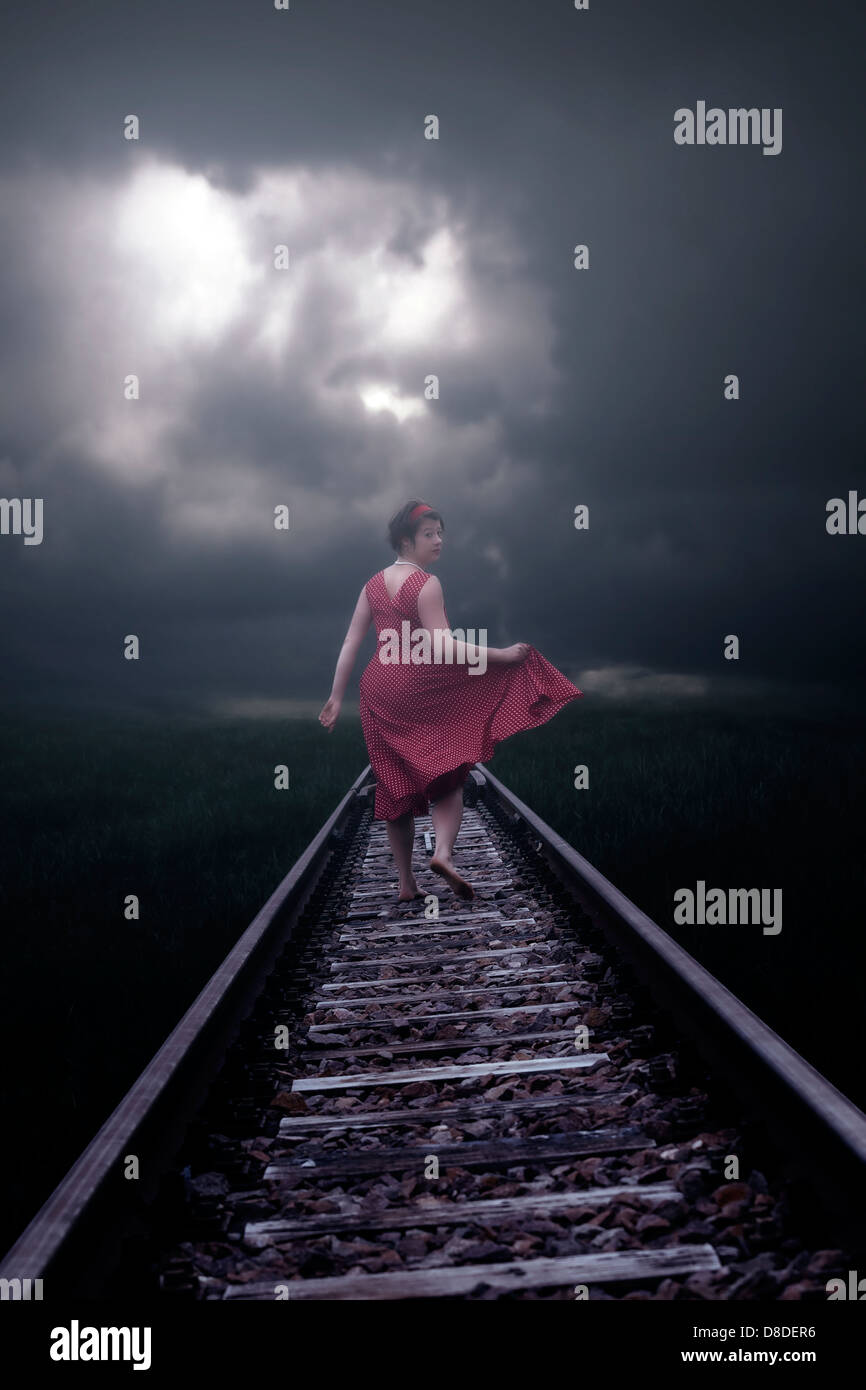 Una ragazza in un abito rosso è in esecuzione su binari ferroviari Foto Stock