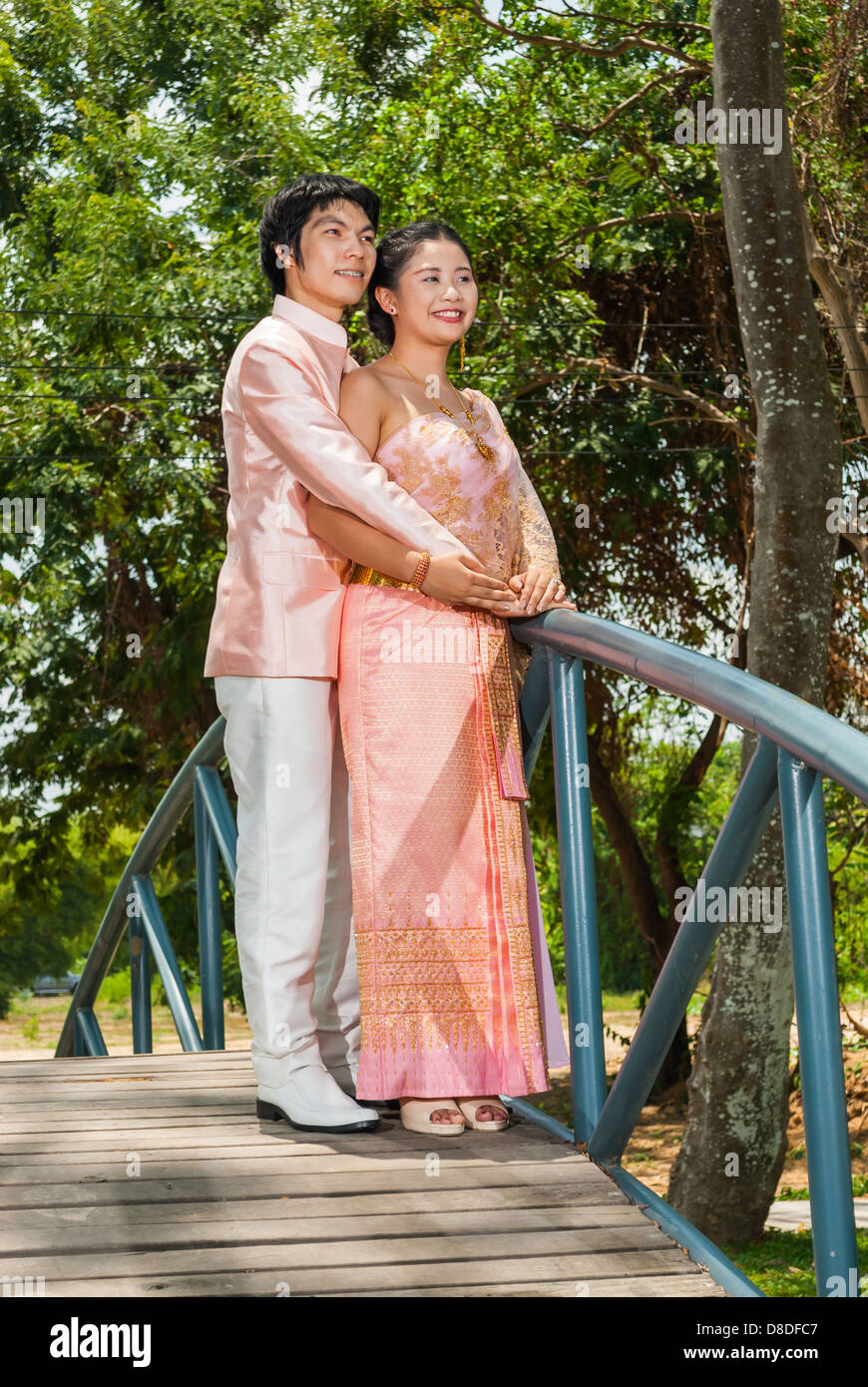 Asian Thai in Nuziale matrimonio Tailandese tuta è in piedi a guardare avanti insieme il futuro accanto a ponte blu. Foto Stock