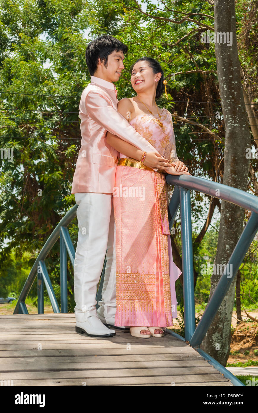 Asian Thai in Nuziale matrimonio Tailandese tuta è in piedi a guardare ogni altra accanto a ponte blu. Foto Stock