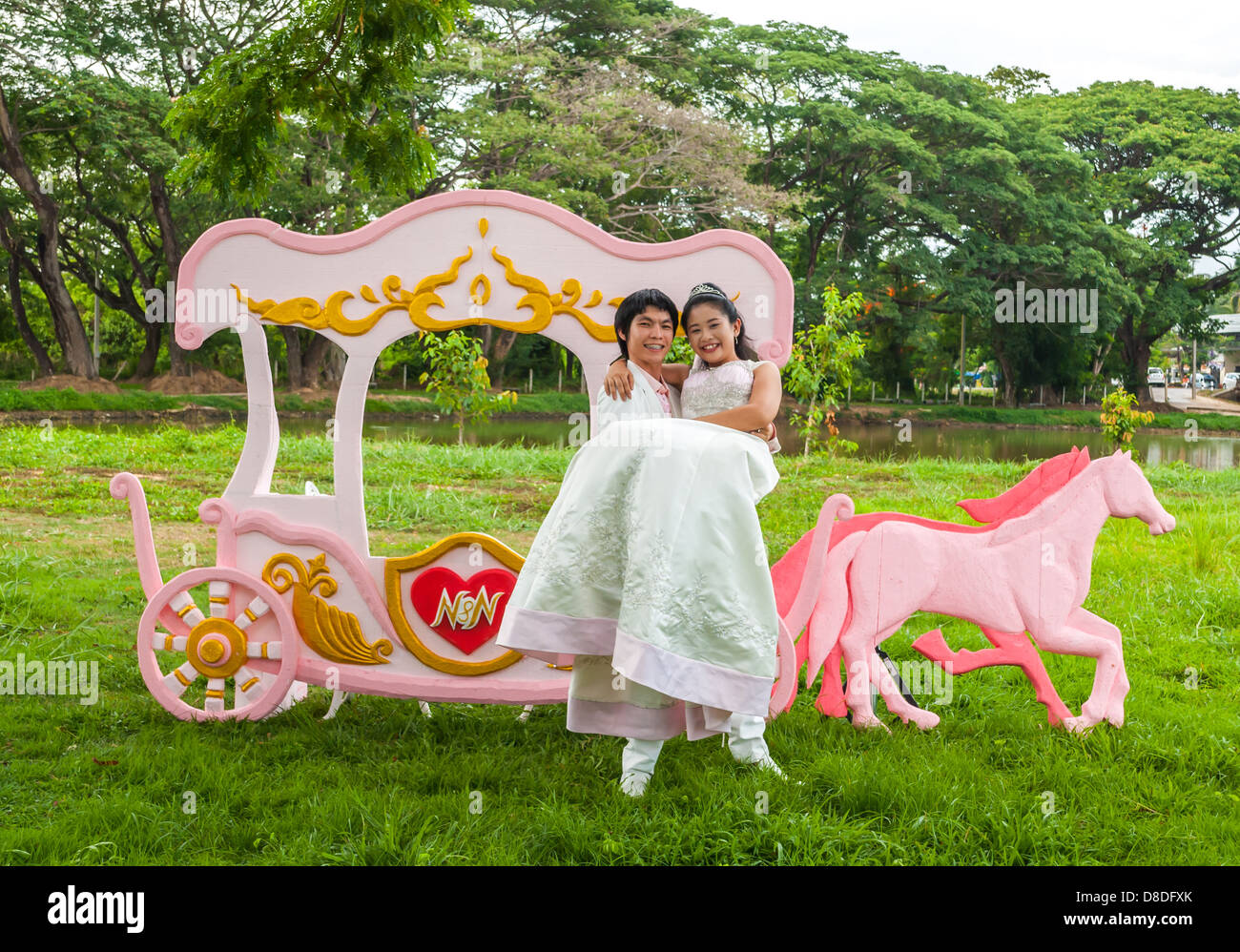 Asian Thai groom sta portando il suo carino sposa nella parte anteriore del carrello romantico con tema d'amore come il principe e la principessa. Foto Stock