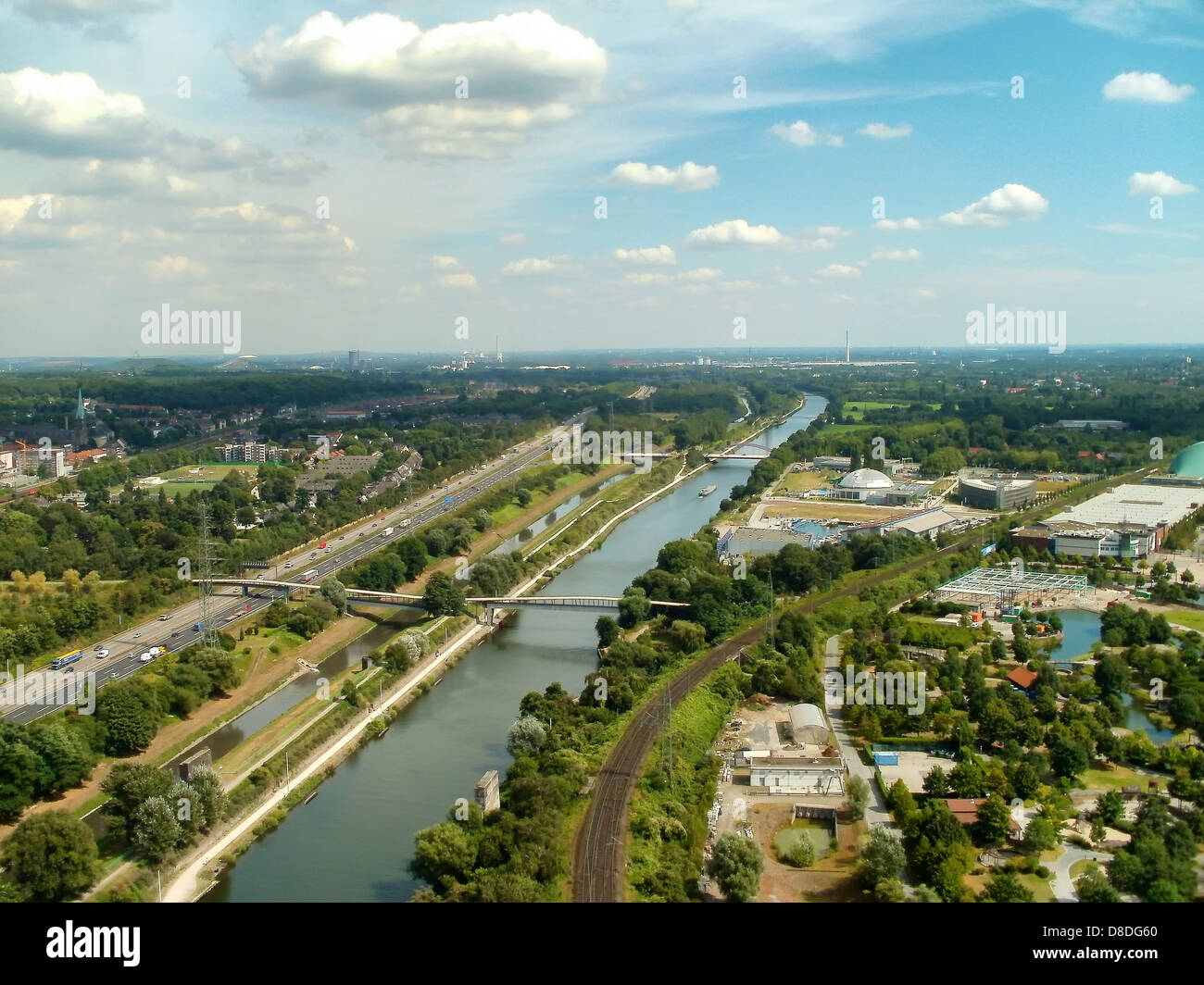Questa vista panoramica di Oberhausen, Germania, mostra una miscela di architettura urbana e paesaggi naturali. L'immagine evidenzia lo skyline della città, il fiume e i ponti, circondati da alberi e un cielo dinamico. Oberhausen è una grande città industriale, conosciuta per i suoi monumenti storici e gli sviluppi moderni, che offre un contrasto visivo unico tra la natura e la vita urbana. Foto Stock