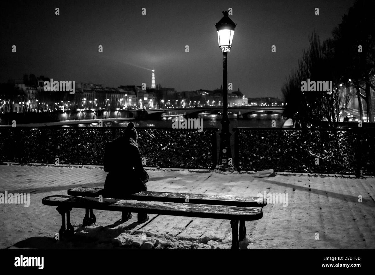 Una donna seduta da sola su una panchina con la Torre Eiffel visibile, sul famoso ponte, Pont des Arts, in una notte di inverni nella neve, Parigi, Francia. Foto Stock