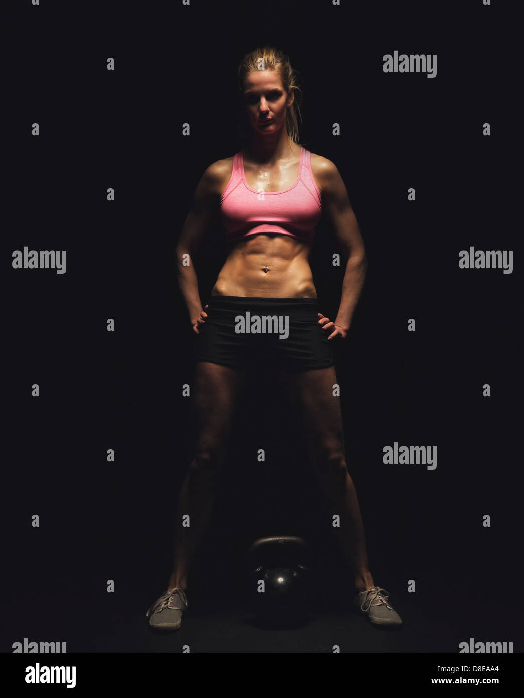 Lunghezza completa di un bodybuilder femminile con kettlebell su sfondo nero Foto Stock