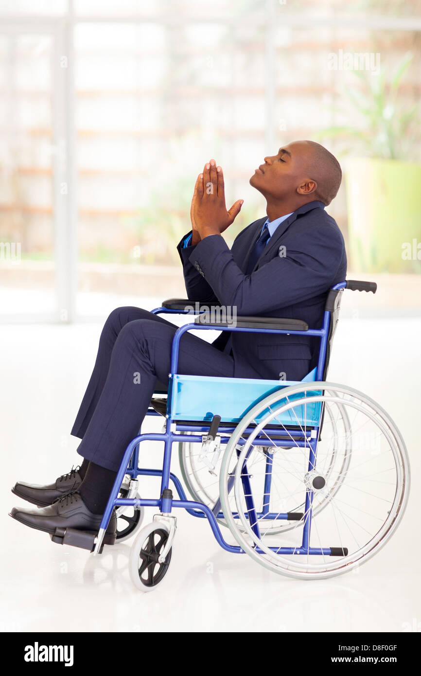 Disabili imprenditore africano seduto su una sedia a rotelle e la preghiera Foto Stock