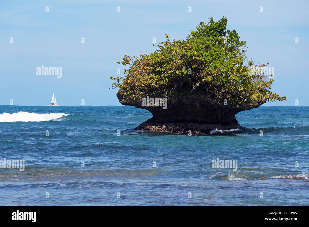 Isolotto roccioso eroso dalle onde con una barca a vela in background, isola Bastimentos, Bocas del Toro, Panama Foto Stock