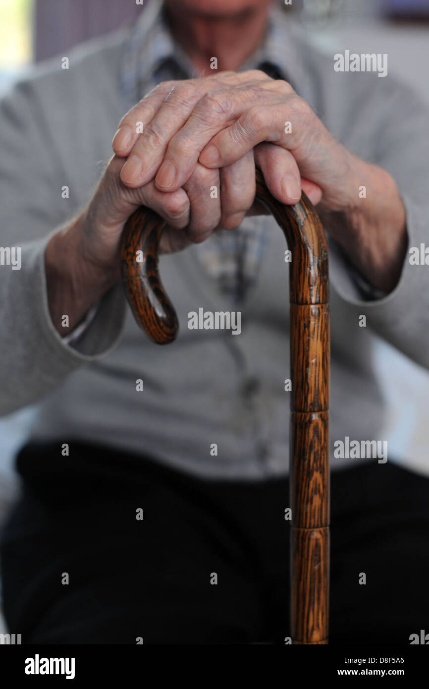 Un anziano vecchiaia titolare di pensione o di rendita si siede con le mani su un bastone da passeggio in una casa di cura. Foto Stock