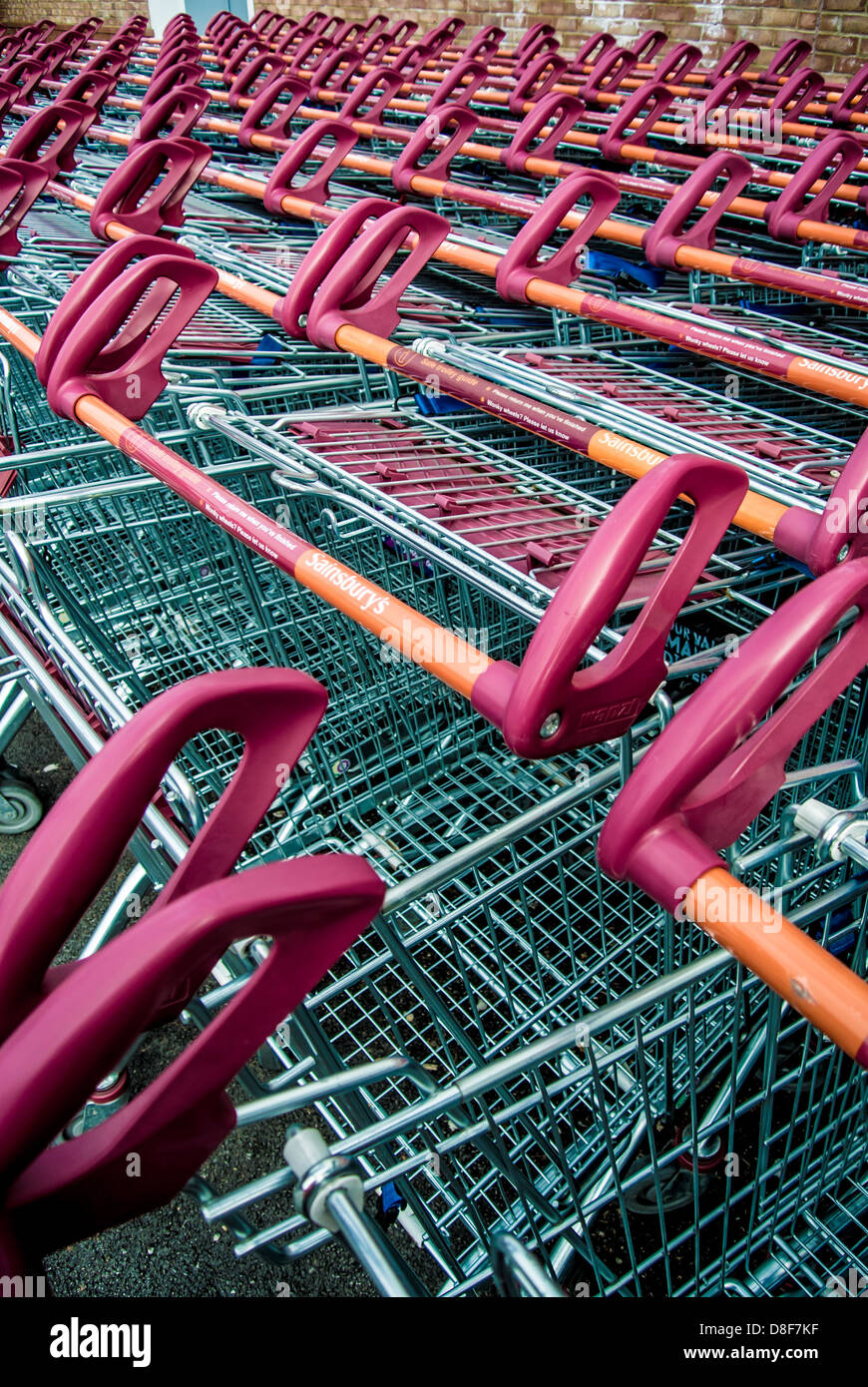 Primo piano delle maniglie arancioni e rosse delle file di carrelli per lo shopping dei supermercati ben parcheggiati fuori dal supermercato Sainsbury's del Regno Unito. Foto Stock