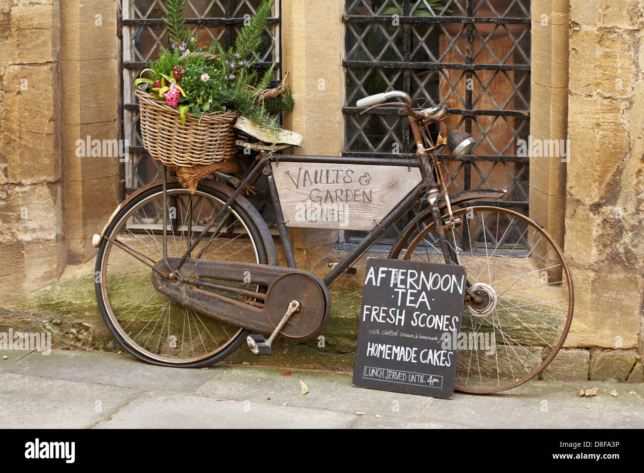 Rust bike con cesto di fiori che fanno pubblicità al tè del pomeriggio focaccine fresche fatte in casa al Vaults & Garden café a Oxford, Oxfordshire Regno Unito nel mese di maggio Foto Stock
