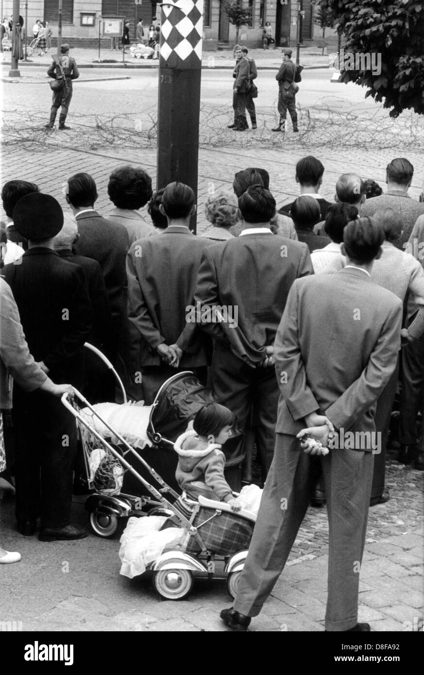 Westberliner Familien am Stacheldrahtverhau in der Bernauer Straße beobachten fassungslos die bewaffneten Volkspolizisten, aufgenommen im Agosto 1961. Am frühen Sonntagmorgen des 13. Agosto 1961 wurde unter der Aufsicht von bewaffneten Streitkräften der DDR mit der Errichtung von Straßensperren Stacheldraht aus dem und Bau einer Mauer begonnen, um den Ostteil berlinese Westteil vom abzusperren. Die Mauer sollte den ständig steigenden Flüchtlingsstrom von Ost- nach Berlino Ovest stoppen Foto Stock