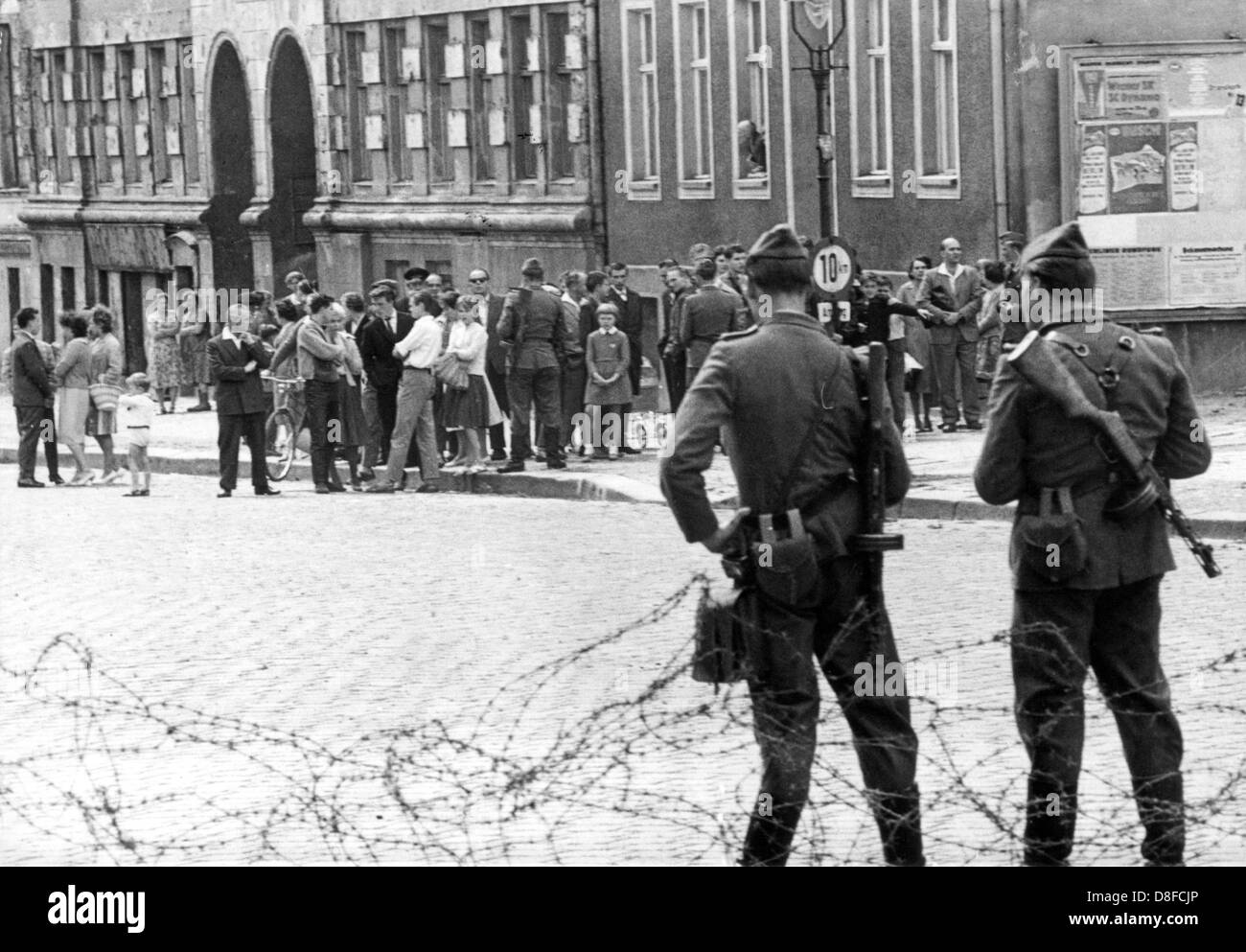 Due poliziotti GDR ("Volkspolizisten') stand di fronte ansiosi a Berlino Est i cittadini su 'Bernauer' Street a Berlino, agosto 1961. Sotto la protezione della RDT forze armate, costruzione squadre hanno cominciato a errect blocchi stradali fatta di filo spinato al fine di barr fuori la parte orientale della città dalla western nelle prime ore del mattino del 13 agosto 1961. Il muro è stato destinato ad arrestare il numero sempre crescente di Tedeschi in fuga da est a ovest. Foto Stock