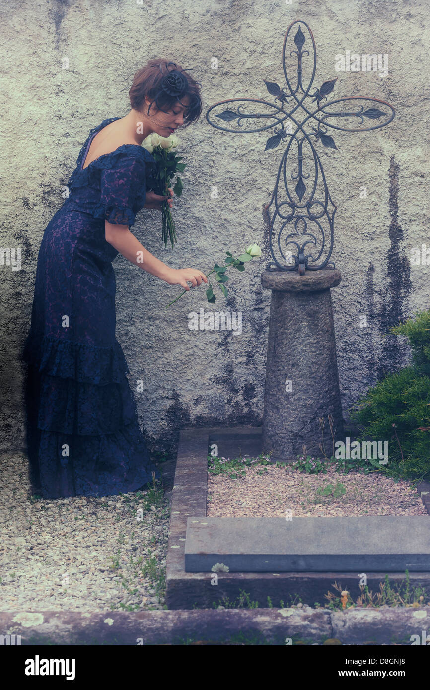 Un dolore di donna con velo e abito scuro su un cimitero, ponendo fiori su una tomba Foto Stock