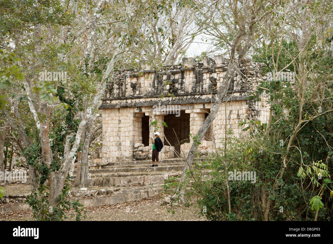 Turista femminile scattare una foto di fronte ad un piccolo tempio Maya avvolto dalla giungla, Uxmal, Yucatan, Messico Foto Stock