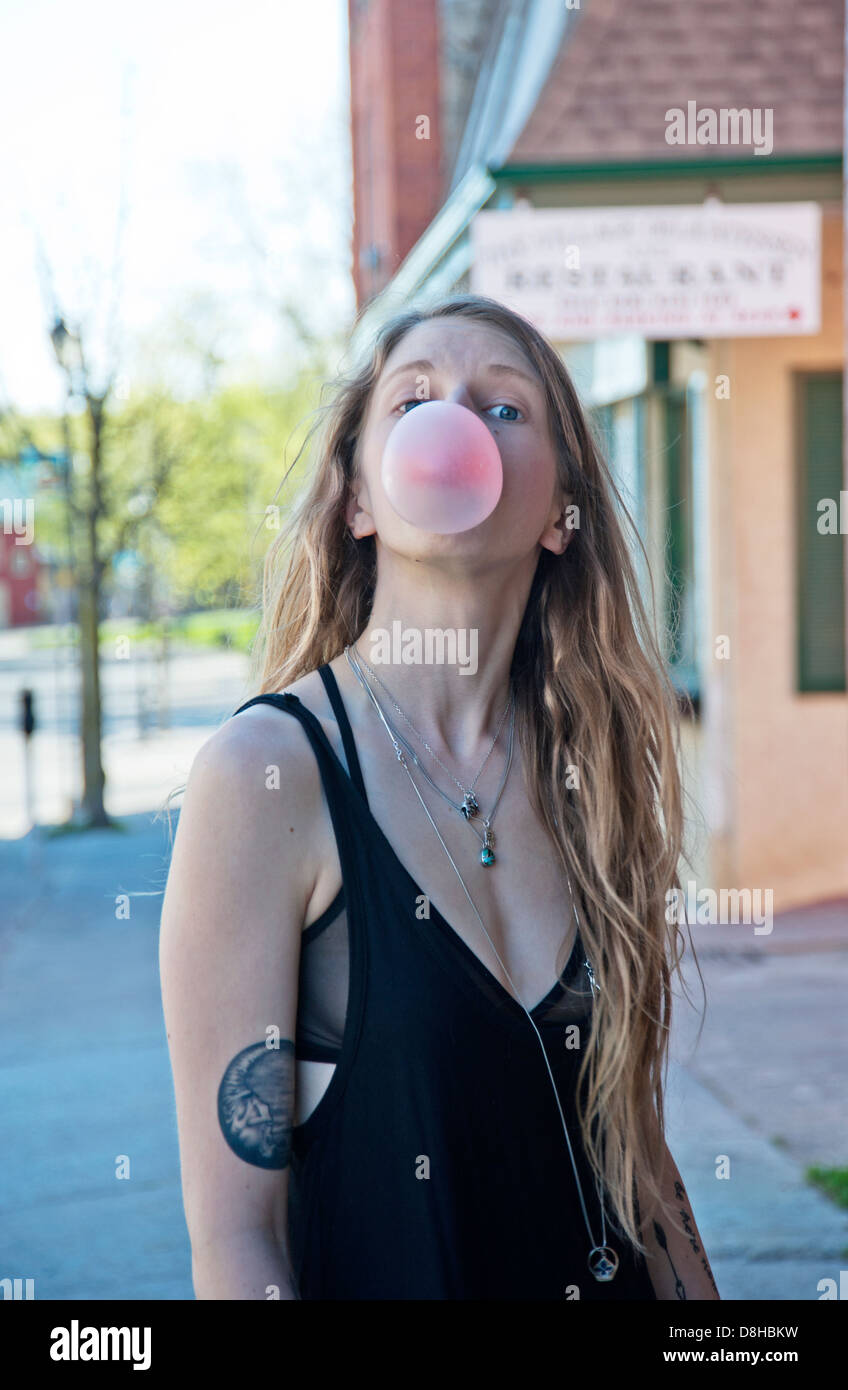 Giovane donna con tatuaggi soffiando bubble gum Foto Stock