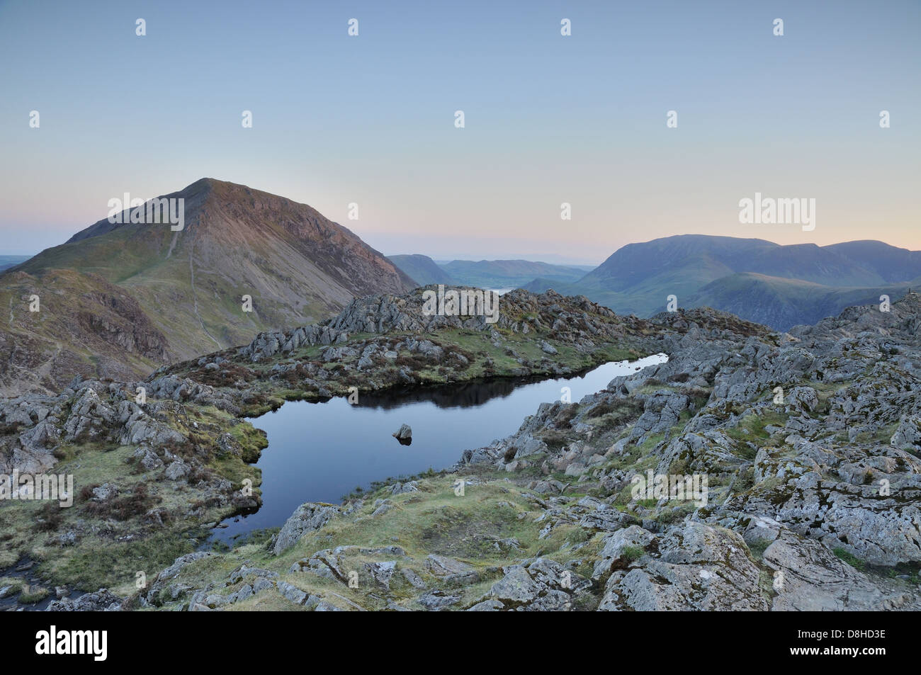 Piccolo tarn sul vertice di Haystacks all'alba nel Lake District inglese, con alta falesia in background Foto Stock