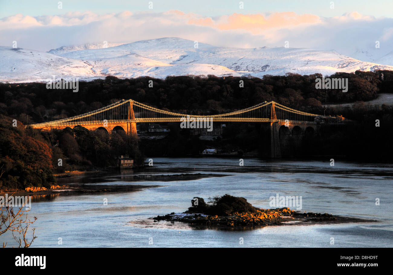La sospensione di Menai Bridge, costruito nel 1826 da Thomas Telford, al tramonto con montagne coperte di neve di Snowdonia in background Foto Stock