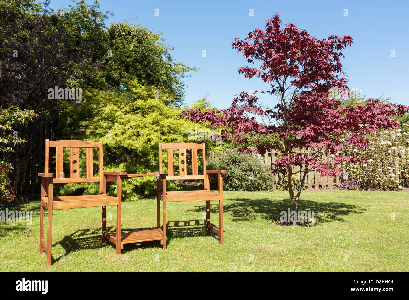 Sedie a panchetta con tavolo tra due posti in legno sostenibile di un albero Acer su un prato domestico giardino posteriore in estate sole. REGNO UNITO Foto Stock