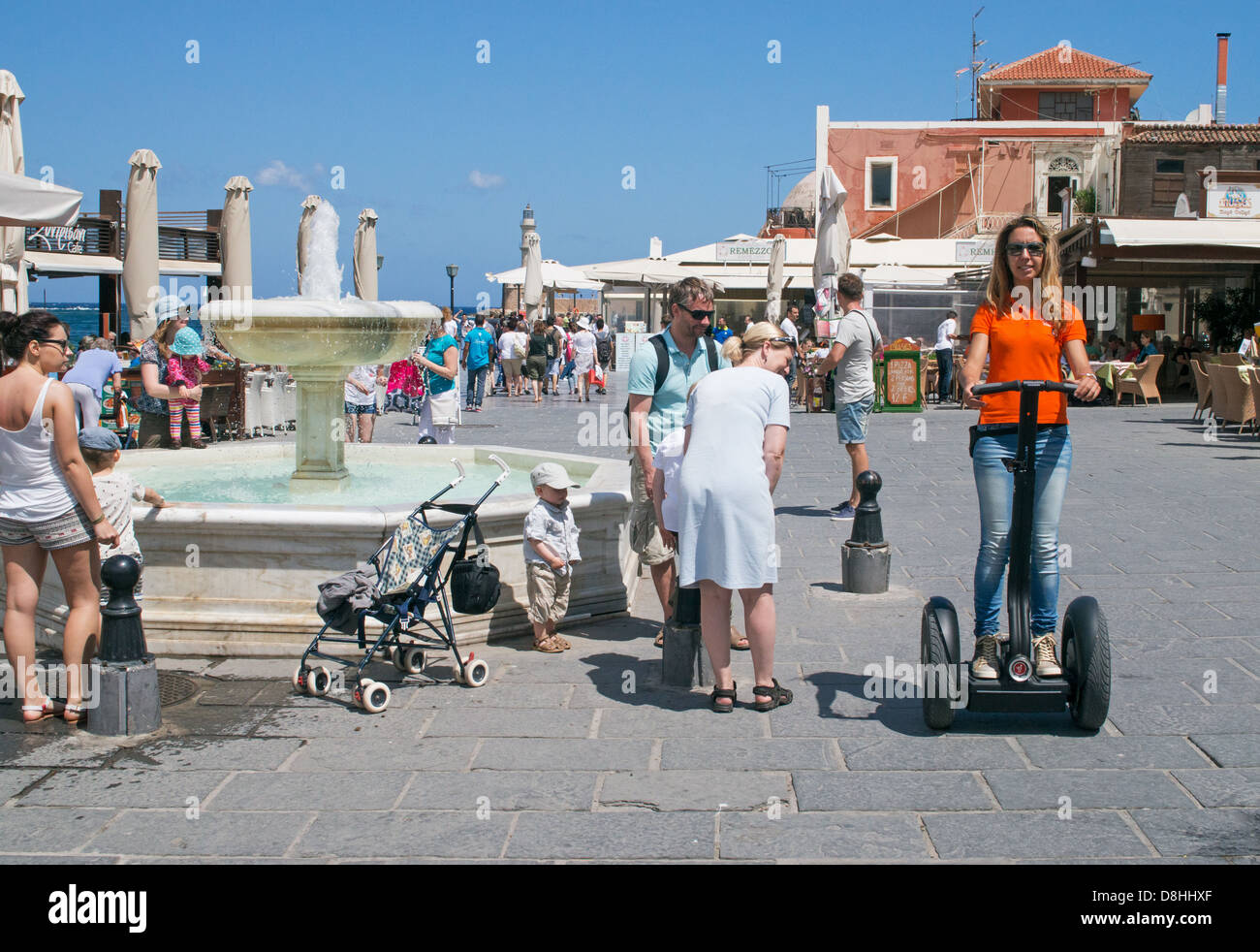 Una giovane donna cavalca un Segway scooter passato la fontana nella piazza del mercato, Chania Creta Foto Stock