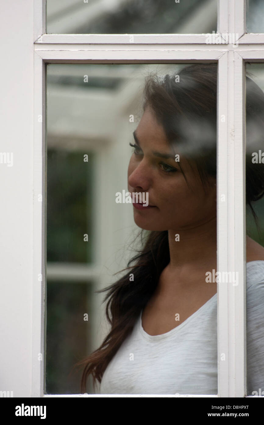 Malinconico giovane donna guardando fuori della finestra Foto Stock