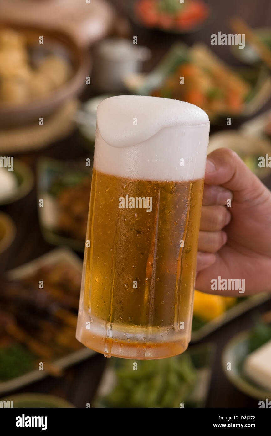 Mano umana azienda boccale di birra a Izakaya Foto Stock