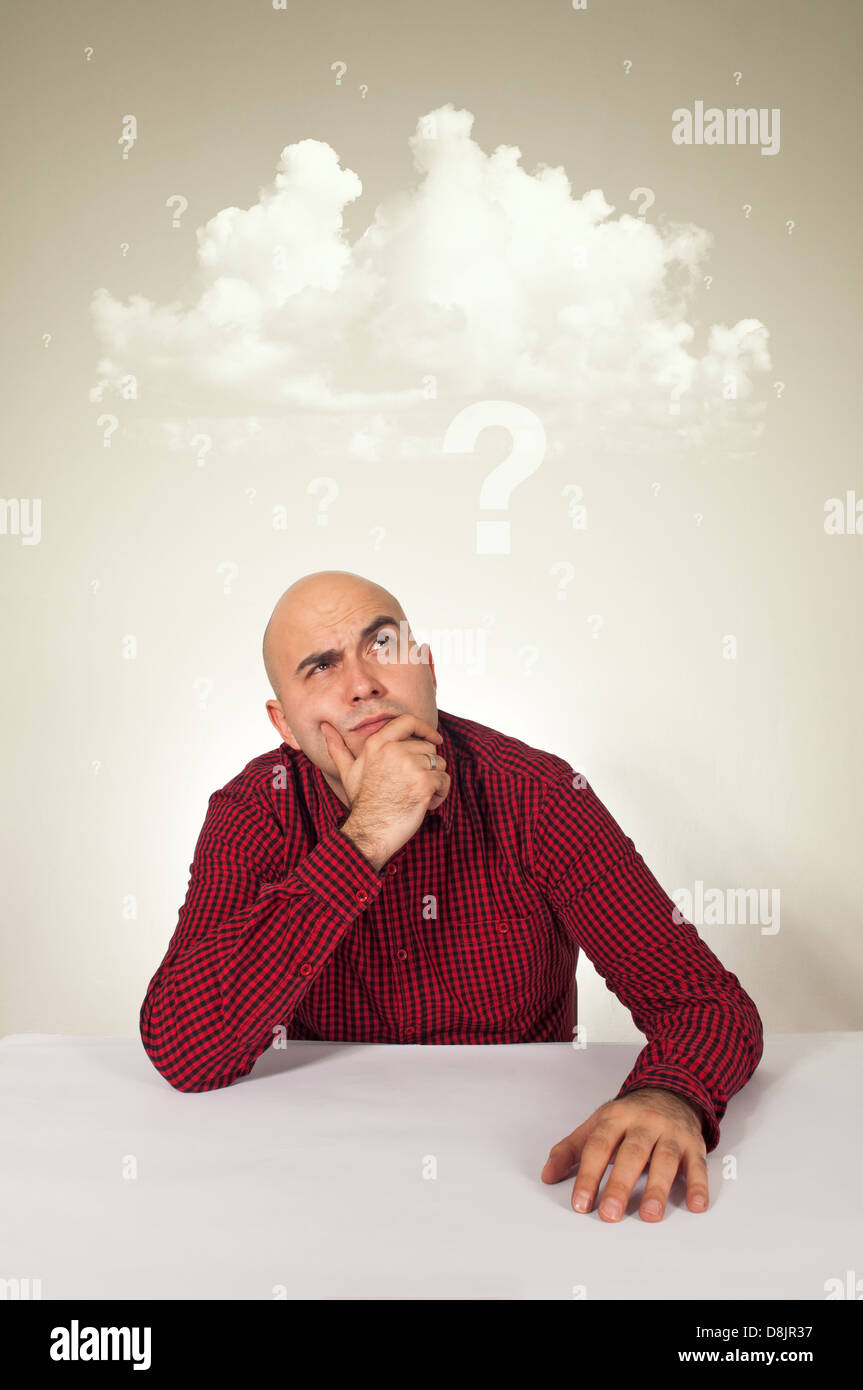 Preoccupato per il giovane adulto uomo calvo di sedere a tavola con la mano  sul suo mento; nuvola di domande sopra la sua testa Foto stock - Alamy