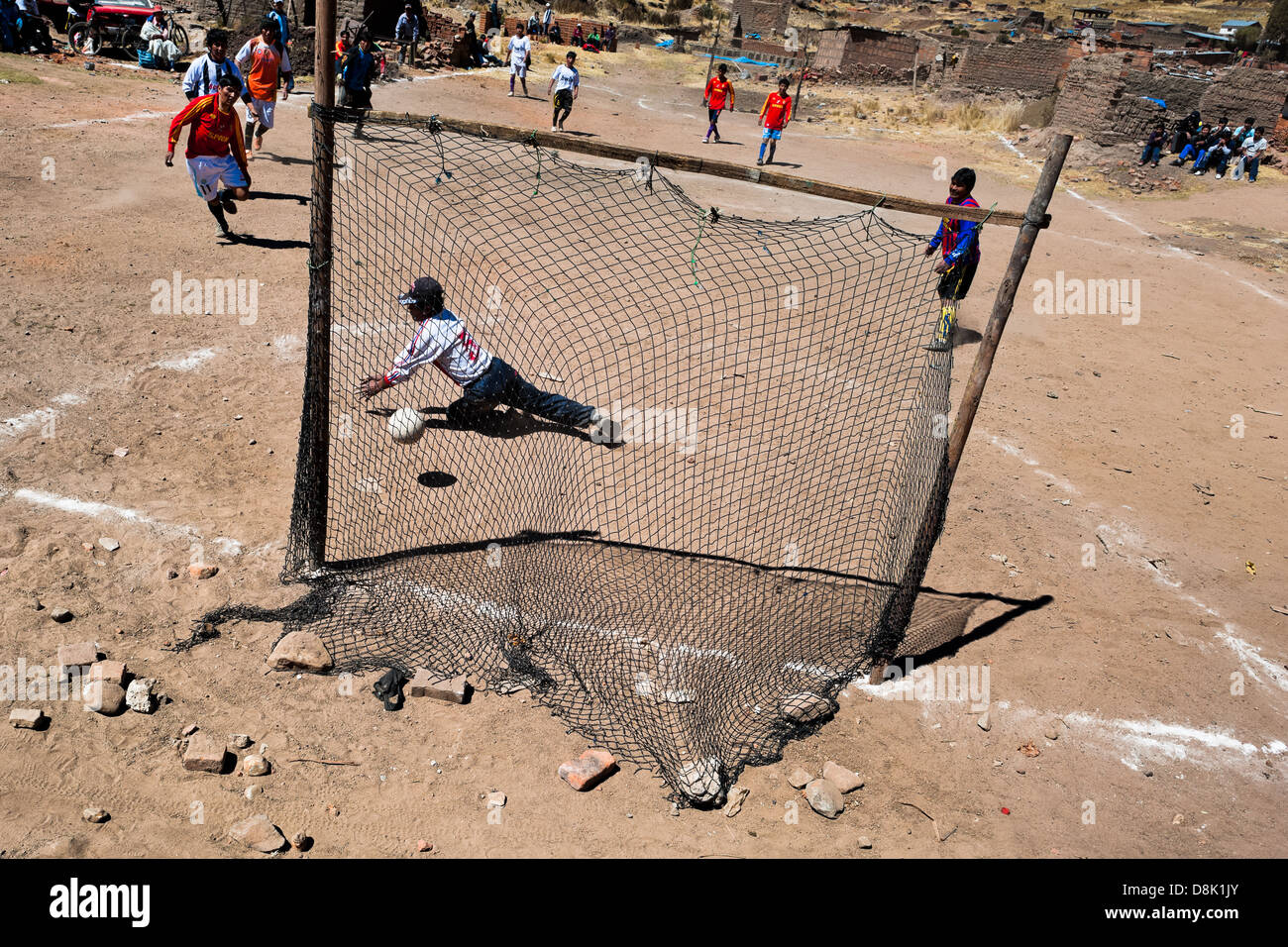 Uomini indigeni giocare a calcio su un polveroso campo di calcio nelle zone rurali della Comunità di montagna vicino a Puno, Perù. Foto Stock