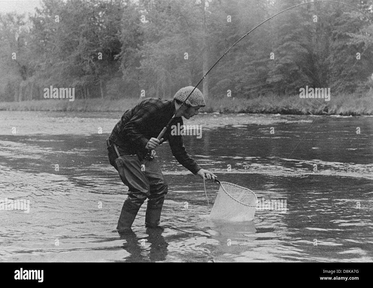 Una fotografia vintage in bianco e nero che mostra un pescatore al lavoro. Il pescatore sta gettando una fila nell'acqua, probabilmente da una piccola barca. L'immagine offre uno sguardo sulle pratiche di pesca tradizionali di un'epoca passata. Foto Stock
