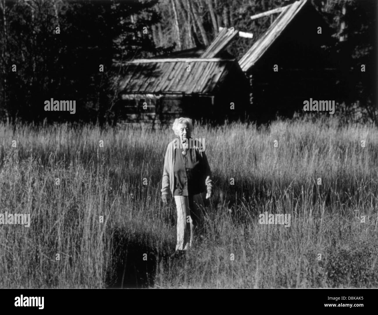 Una foto in stile vintage di una donna anziana in piedi accanto a un vecchio fienile, che cattura un momento nel tempo. I toni sbiaditi e lo sfondo rustico evocano nostalgia e il passare del tempo. Foto Stock