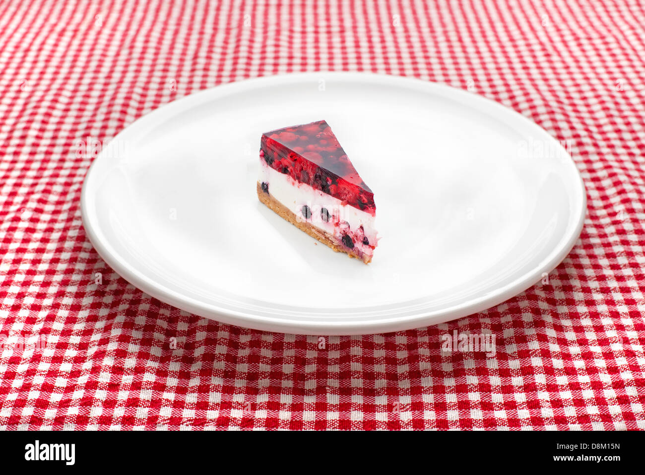 Torta di formaggio sulla piastra bianca su un tavolo da cucina, rosso e bianco tovaglia a scacchi in background. Foto Stock